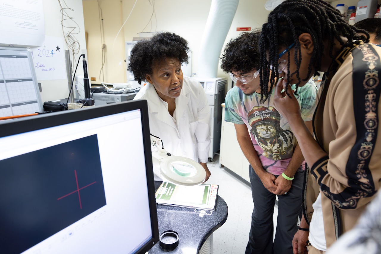 Students and researchers collaborating around a computer and lab equipment in a quantum laboratory