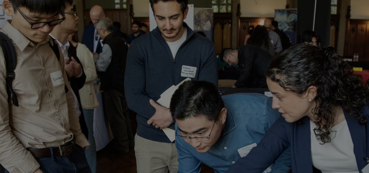 Darkened inmage of people gathered around a table with a laptop at an event, with an "IBM Quantum" sign.