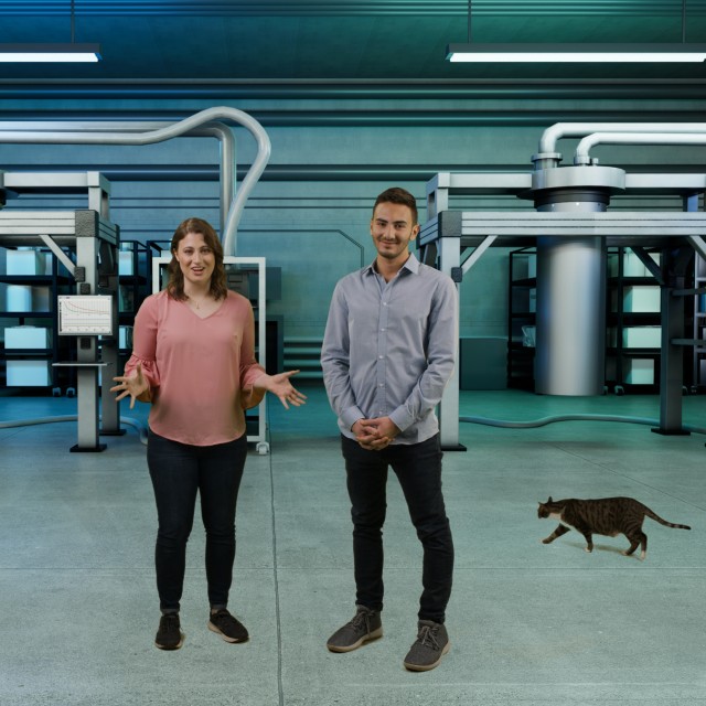 Photo of Robert Weinbaum and Katie Sautter in a futuristic lab background with a dilution fridge and optical table. A cat is walking behind them. 