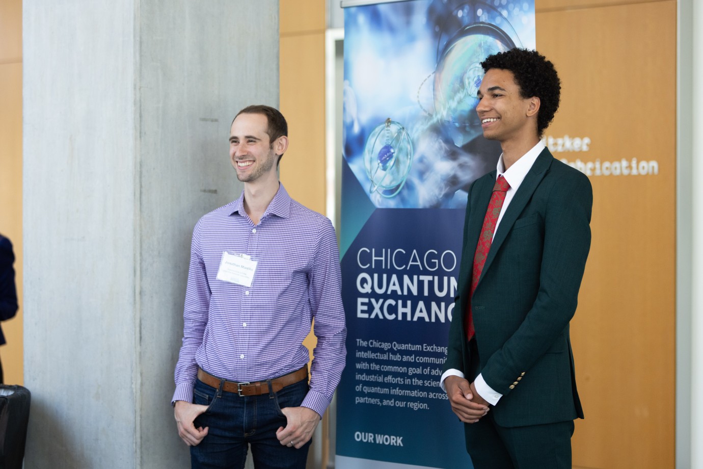 Peter and industry partner at the OQI research symposium posing in front of the CQE banner.