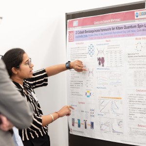 A woman presenting a scientific poster at a conference to an audience.