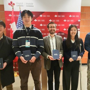 Five individuals holding Chicago Quantum Exchange notebooks in front of a banner for Invest Canada.