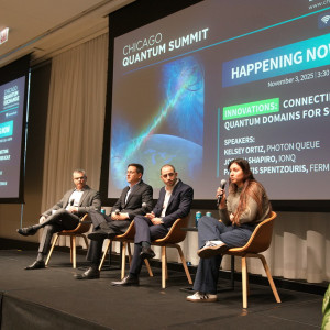 Four panelists seated on stage at the Chicago Quantum Summit with a large screen displaying event details in the background.