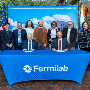 A group of people in a signing ceremony at a table with the Fermilab logo.