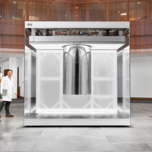 A large glass and metal structure, IBM Quantum System One, in a modern interior with people walking nearby.