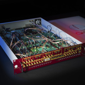 Open modular synthesizer with green circuit boards, multicolored patch cables, and a red control panel in a white enclosure.