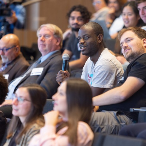 Victroy Omole, from Infleqtion, sits in a crowd of people holding a microphone at the 2022 Chicago Quantum Summit