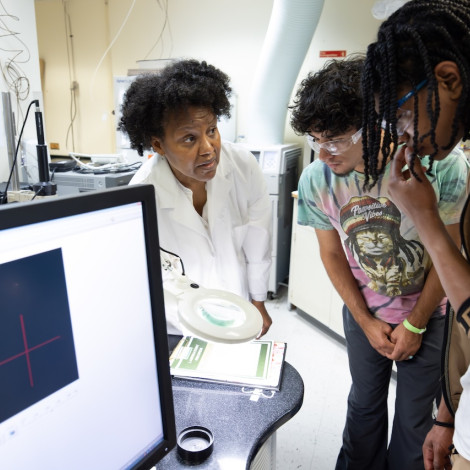 A group of people in a laboratory setting, focusing on a discussion around a computer and lab equipment.
